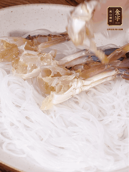 盤底墊上粉絲，擺上梭子蟹、火腿片，撒姜粒，淋上蒸魚豉油、花雕酒調味腌制15分鐘